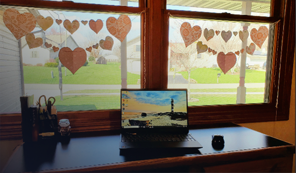 Home office with desk and laptop computer and pencil case, under windows looking out to a green lawn and a residential neighborhood